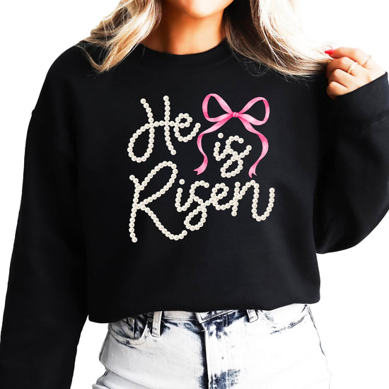 Close-up view of pearl He Is Risen text with decorative bow on green pullover sweatshirt