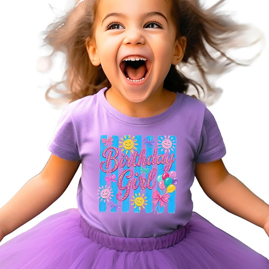Birthday Girl tee flat lay showing full design with brushstroke stripes, pink bows, and smiling sun graphics