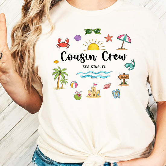 Product mockup showing Cousin Crew beach shirt design with coastal elements and typography