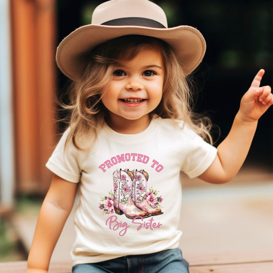 Big Sister shirt flat lay displaying full pink cowgirl boots and floral design