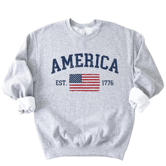 Close-up of America Est 1776 sweatshirt showing weathered American flag design with stars and stripes