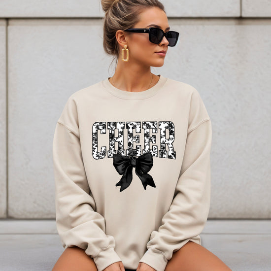 Sand cheer sweatshirt with black floral bow design, styled view