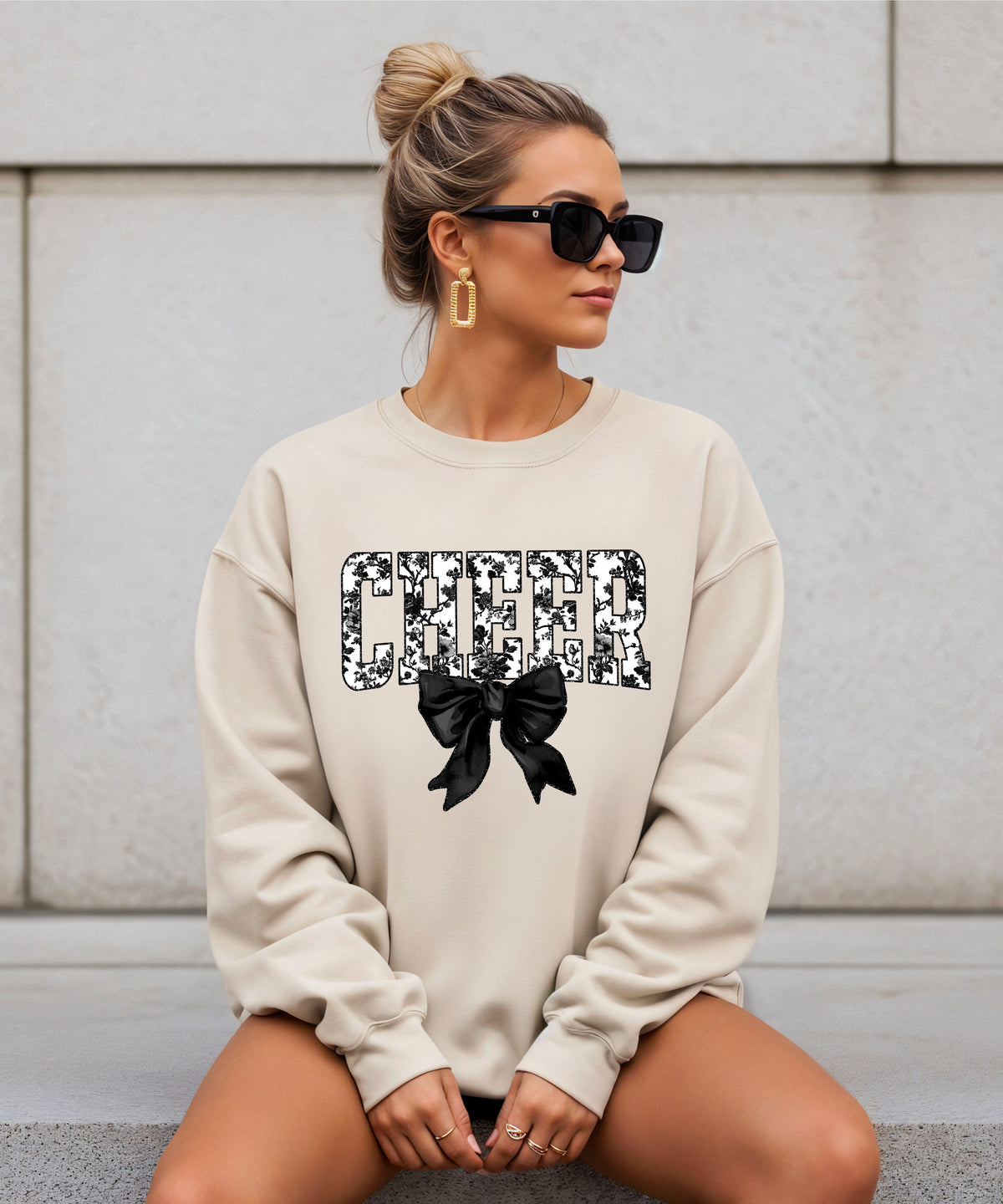 Sand cheer sweatshirt with black floral bow design, styled view