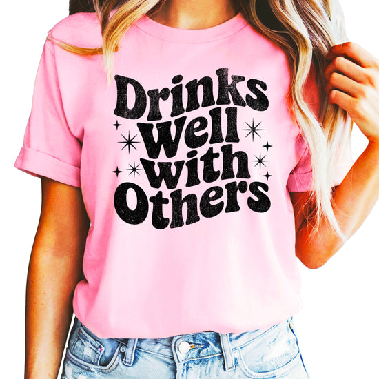 Drinks Well With Others funny graphic tee for women in Pink, front view