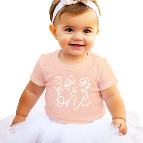 Floral One first birthday shirt for baby girls in white on peach, front view