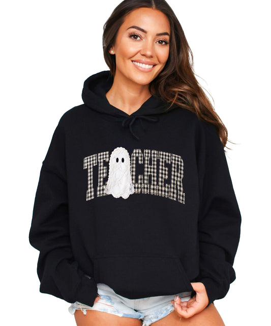 Black hoodie with ink-printed gingham ghost teacher Halloween graphic, front view