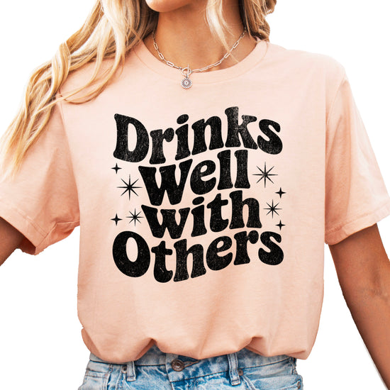 Drinks Well With Others funny graphic tee for women in Peach, front view
