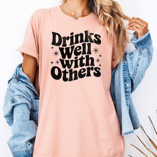 Drinks Well With Others funny graphic tee for women in Peach, back view