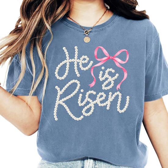 Front view of He Is Risen Christian shirt for women featuring pearl bow faith graphic on light tee