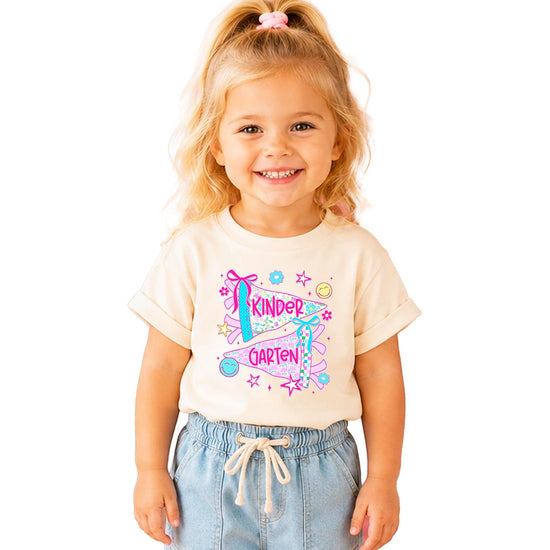 Girls kindergarten graphic tee with coquette-bow pennants, pink lettering, retro flowers, and shooting stars on natural cotton