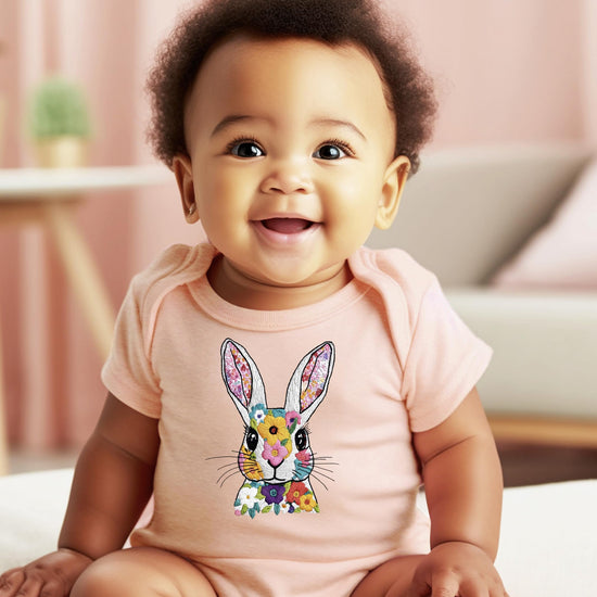 Peach baby girl snap bodysuit with pastel floral bunny graphic on white background