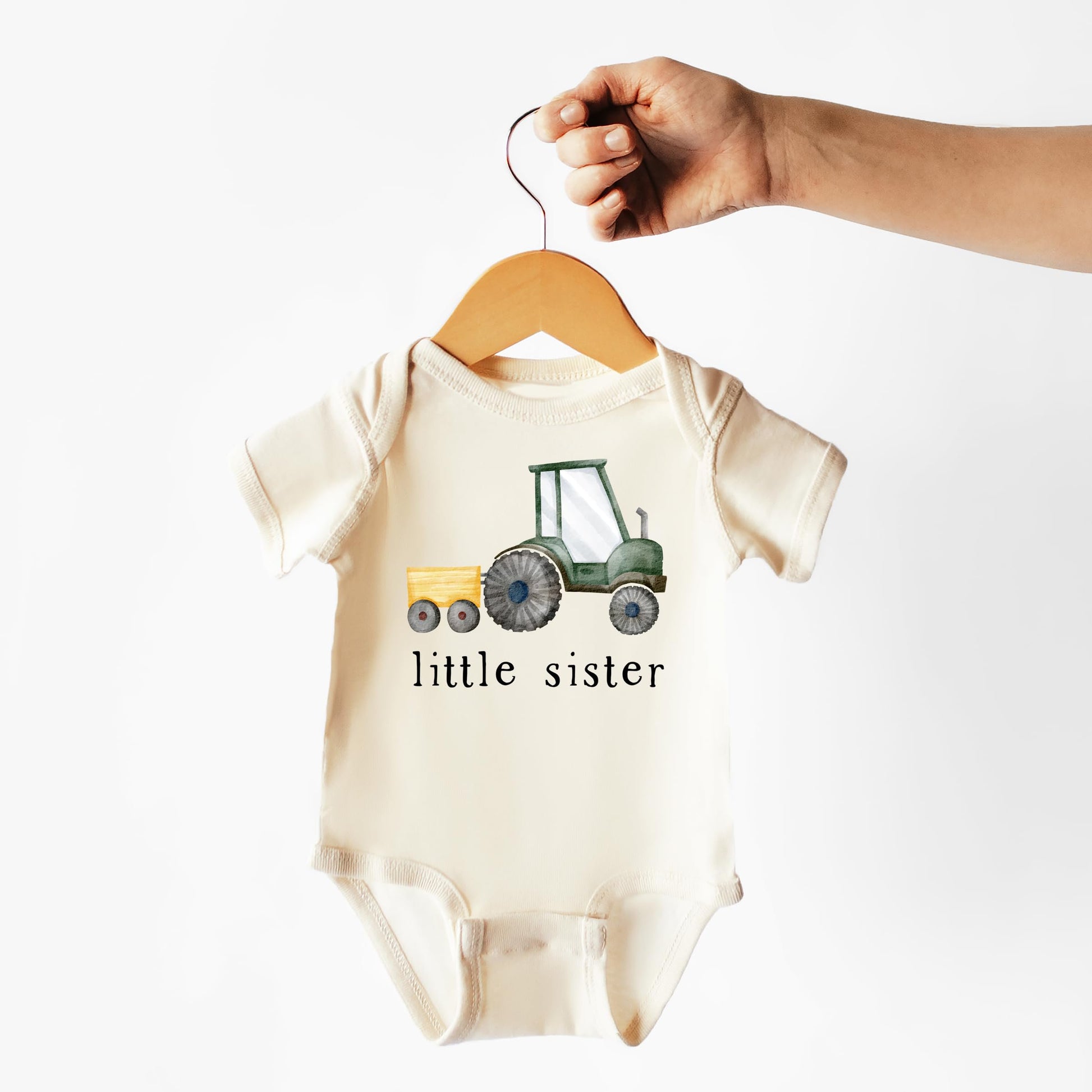 Baby girl wearing little sister farm tractor bodysuit laid flat on neutral background