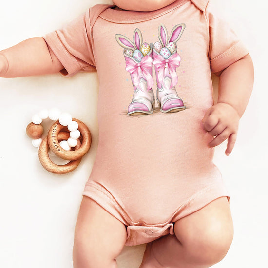 Flat lay of western-themed Easter baby bodysuit in peach and pink tones for newborn girls