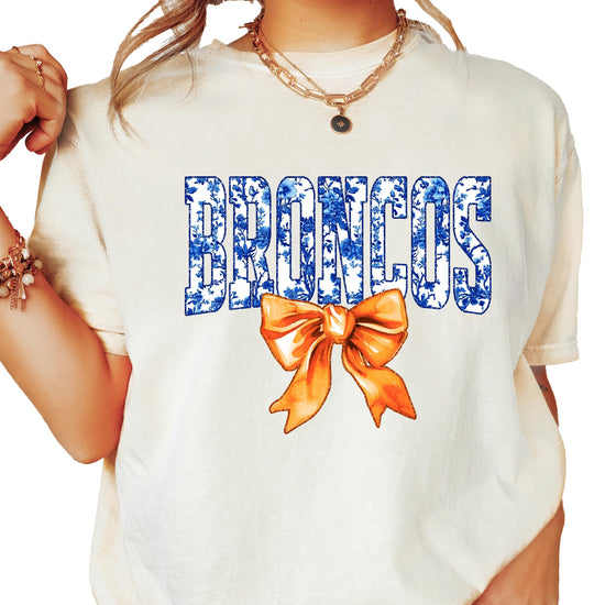Broncos fan shirt flat lay showing blue floral lettering and orange bow on women's tee