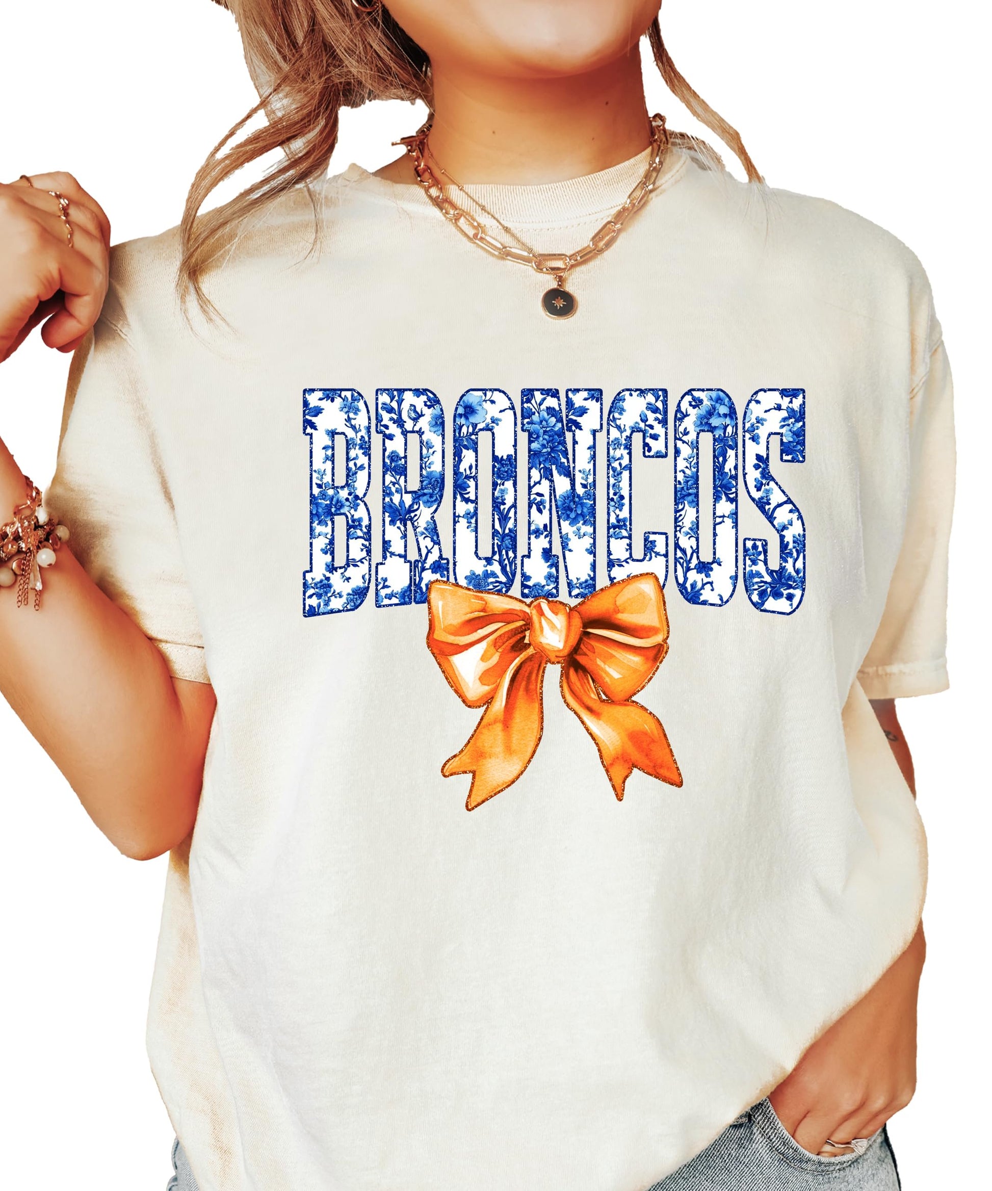 Broncos fan shirt flat lay showing blue floral lettering and orange bow on women's tee