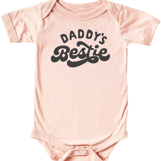 Close-up of Daddy's Bestie retro graphic print on a soft peach baby one-piece bodysuit