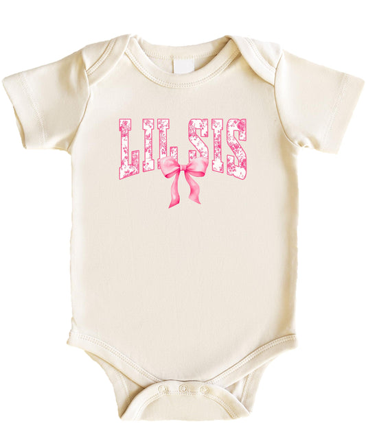 Close-up of floral graphic and pink bow design on a natural one-piece baby bodysuit