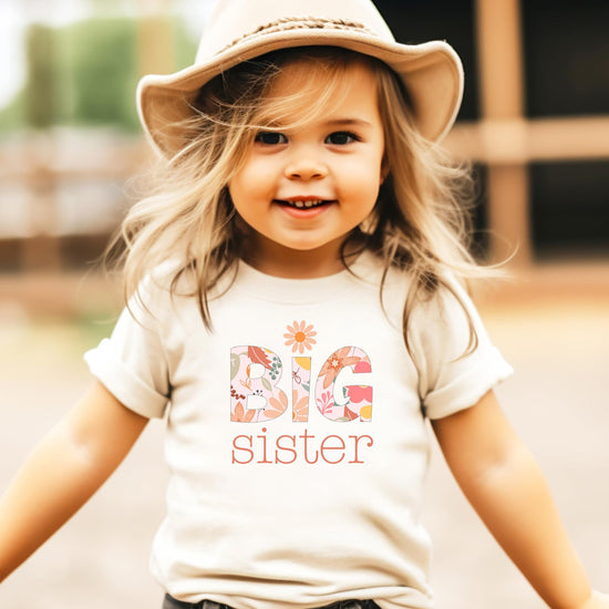 Toddler girl in a girly floral Big Sister shirt with daisy graphic in soft colors
