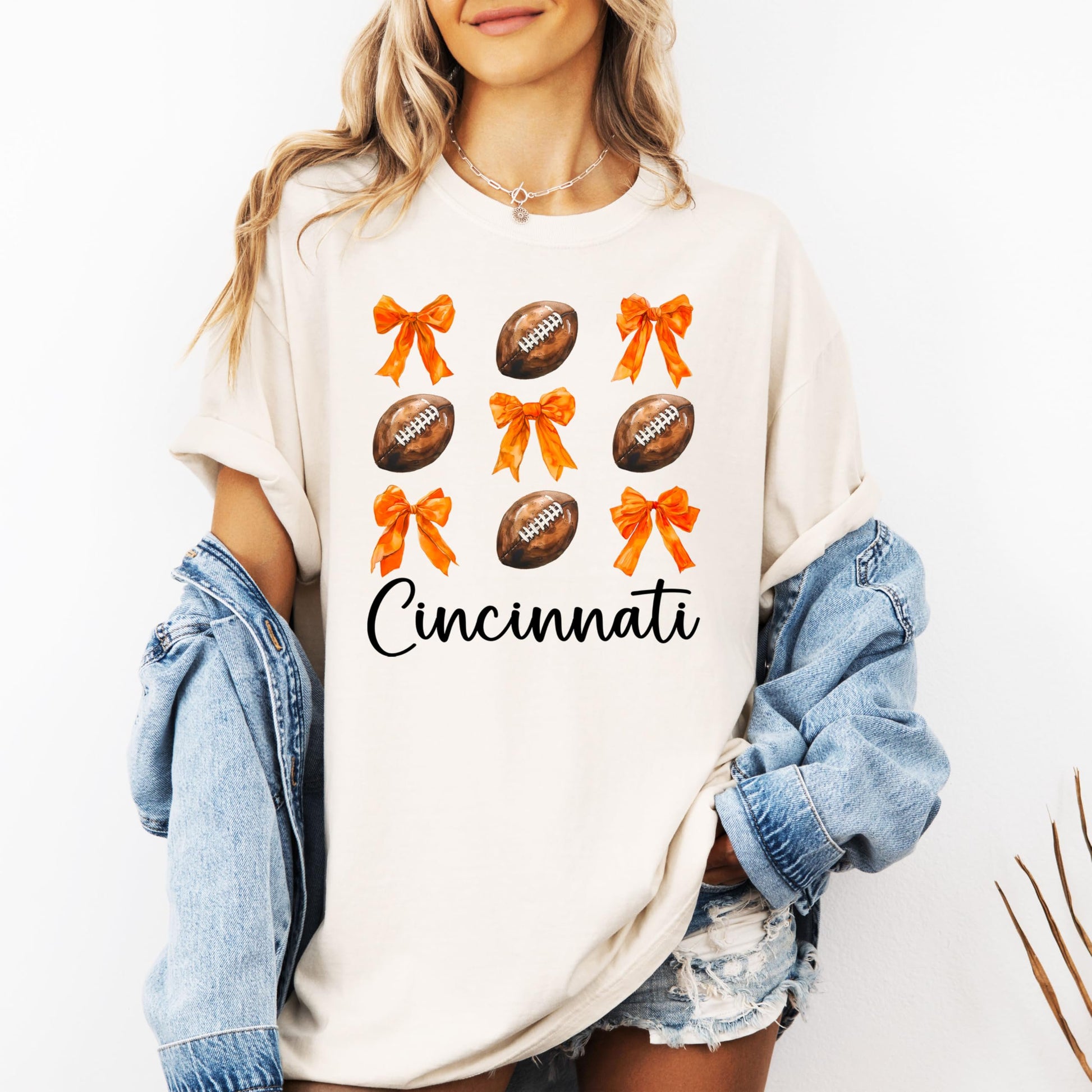 Women's ivory Cincinnati football tee laid flat showing full girly orange bows and footballs design