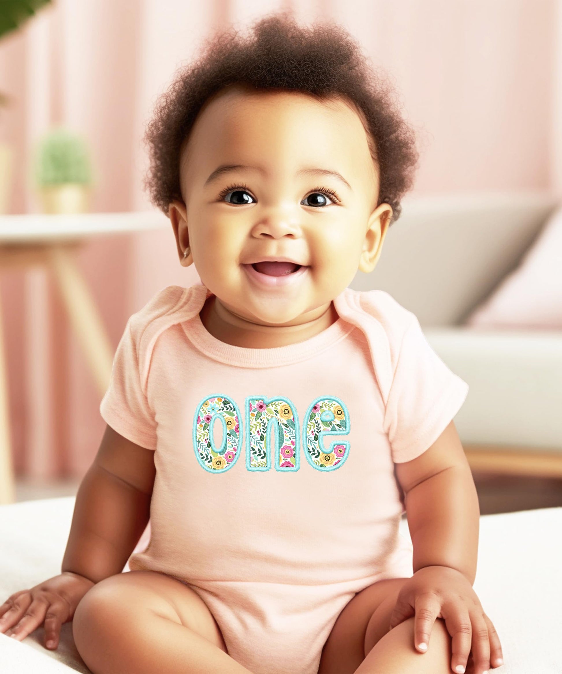 Close-up of teal embroidered floral lettering on peach 1st birthday baby girl bodysuit