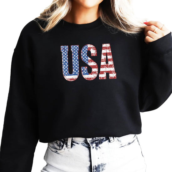 Black patriotic crewneck sweatshirt with vintage-style USA flag design, styled flat lay