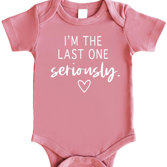 Flat lay of funny last baby bodysuit in white on mauve styling for newborn coming home outfit