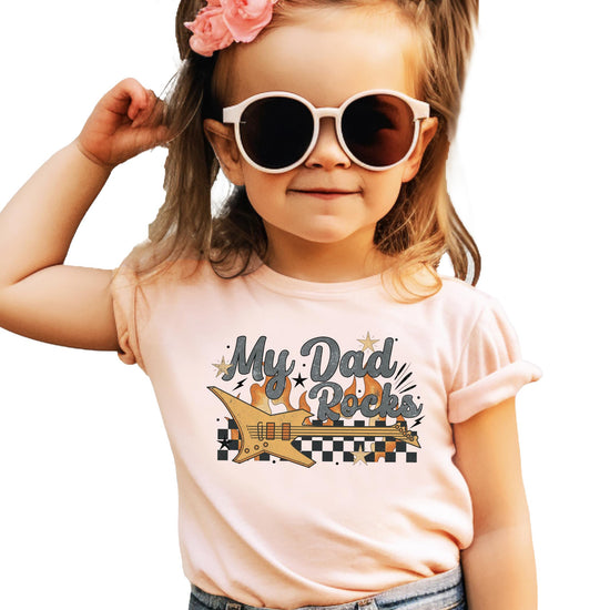 My Dad Rocks kids' graphic tee with electric guitar, flames, and checkered pattern on peach shirt