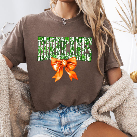 Hurricanes school pride women's graphic tee in ivory with bold green floral lettering and orange bow