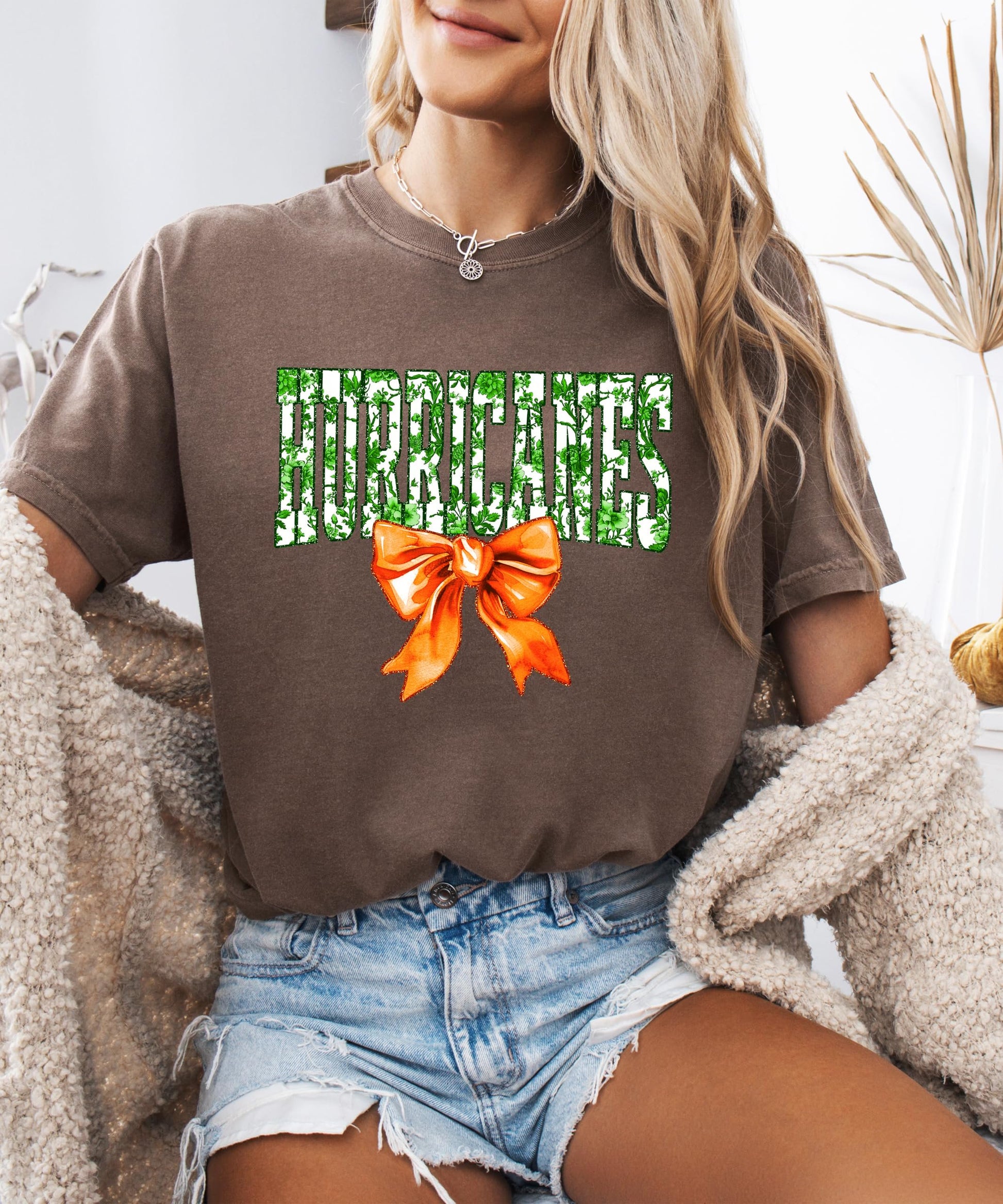 Hurricanes school pride women's graphic tee in ivory with bold green floral lettering and orange bow