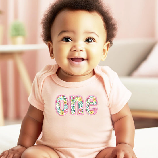Close-up of floral one graphic on pink baby girl first birthday bodysuit showing colorful flower details