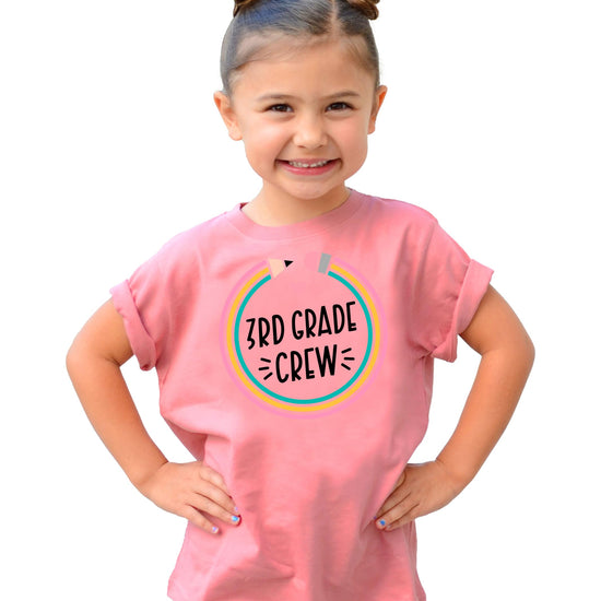 Front view of youth mauve 3rd Grade Crew pencil shirt on flat lay background