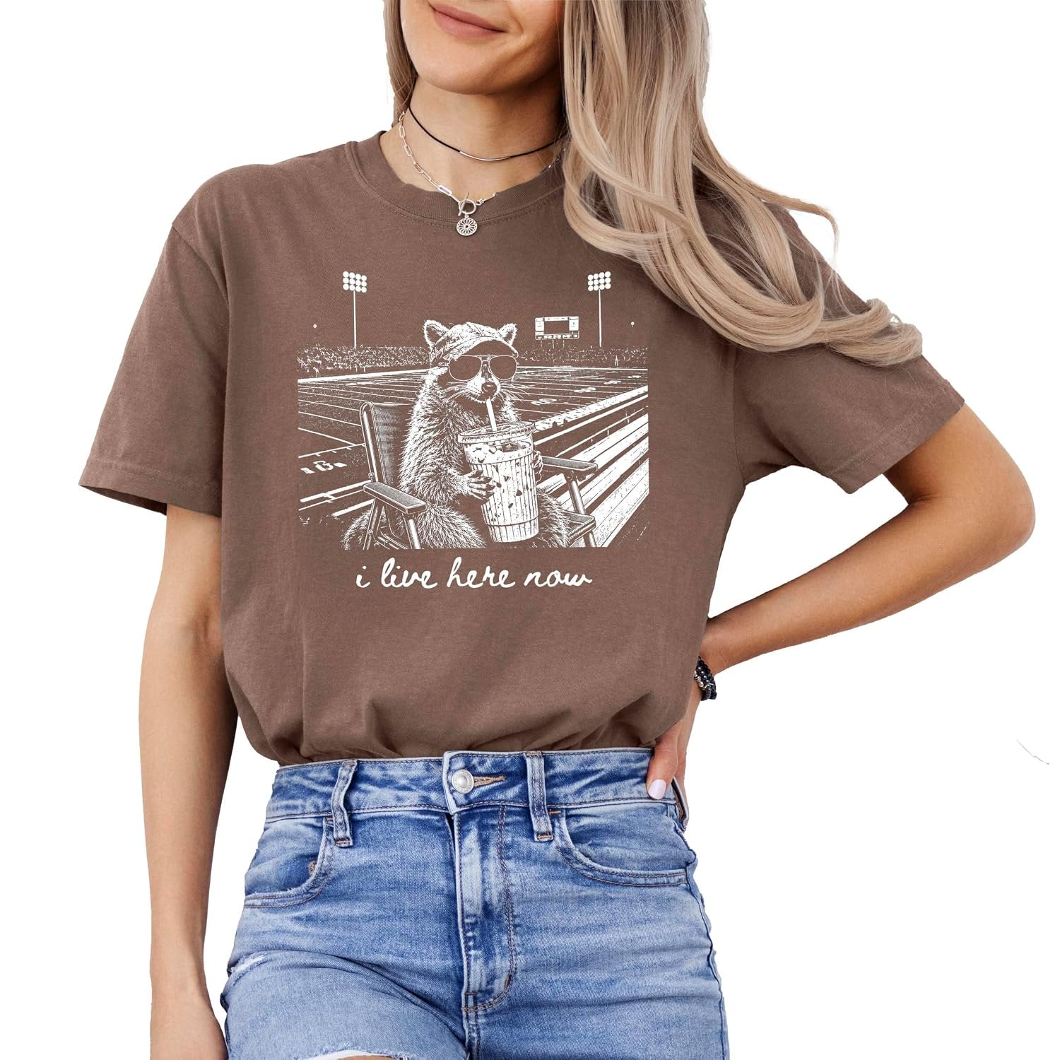 Flat lay of Comfort Colors I Live Here Now raccoon football mom tee showing full print detail