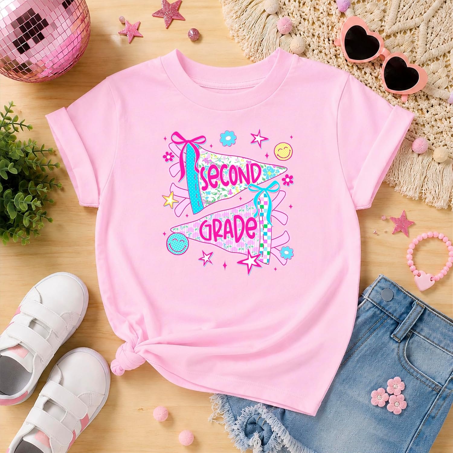 Detail shot of bold pink Second Grade pennant lettering with coquette bow accents on kids graphic tee
