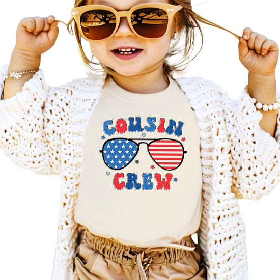 Peach colored youth t-shirt with Cousin Crew text and patriotic sunglasses design in red white and blue