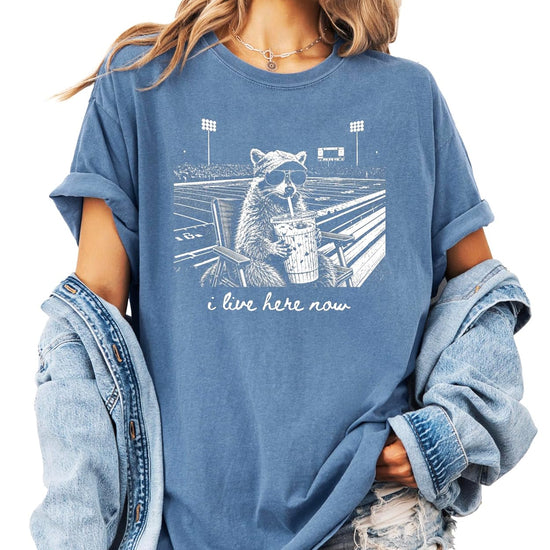 I Live Here Now funny raccoon football mom graphic tee in garment-dyed Comfort Colors, front view