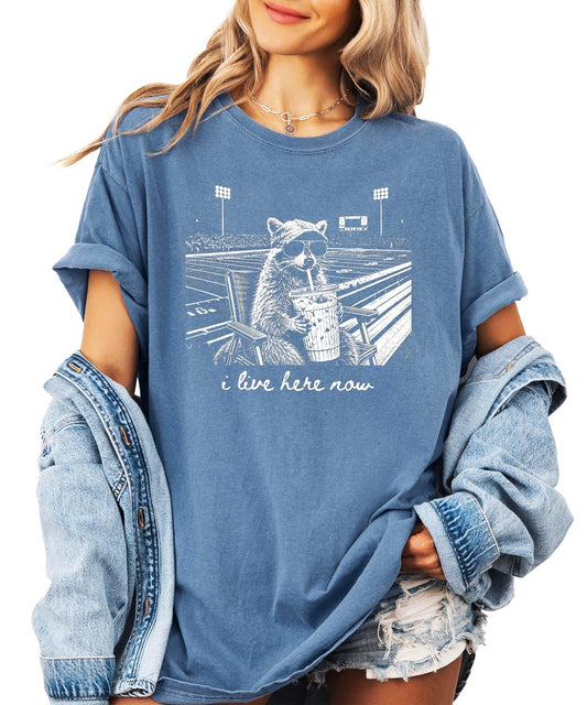 I Live Here Now funny raccoon football mom graphic tee in garment-dyed Comfort Colors, front view