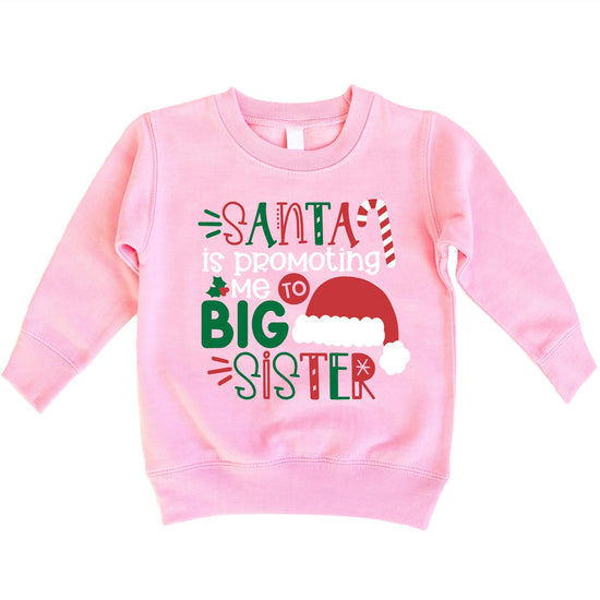 Toddler girl wearing a heather natural sweatshirt with 'Promoted to Big Sister' Santa holiday graphic print