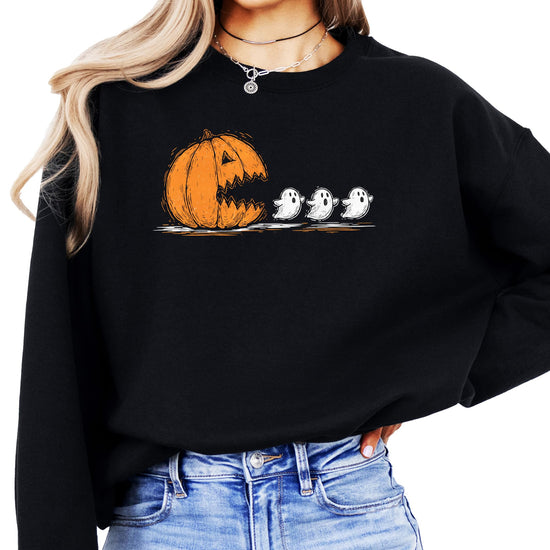 Women wearing a cozy Halloween sweatshirt with a carved pumpkin chomping ghosts graphic