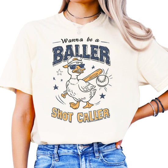 Ivory baseball shirt with "Wanna Be A Baller Shot Caller" text and cartoon duck graphic design