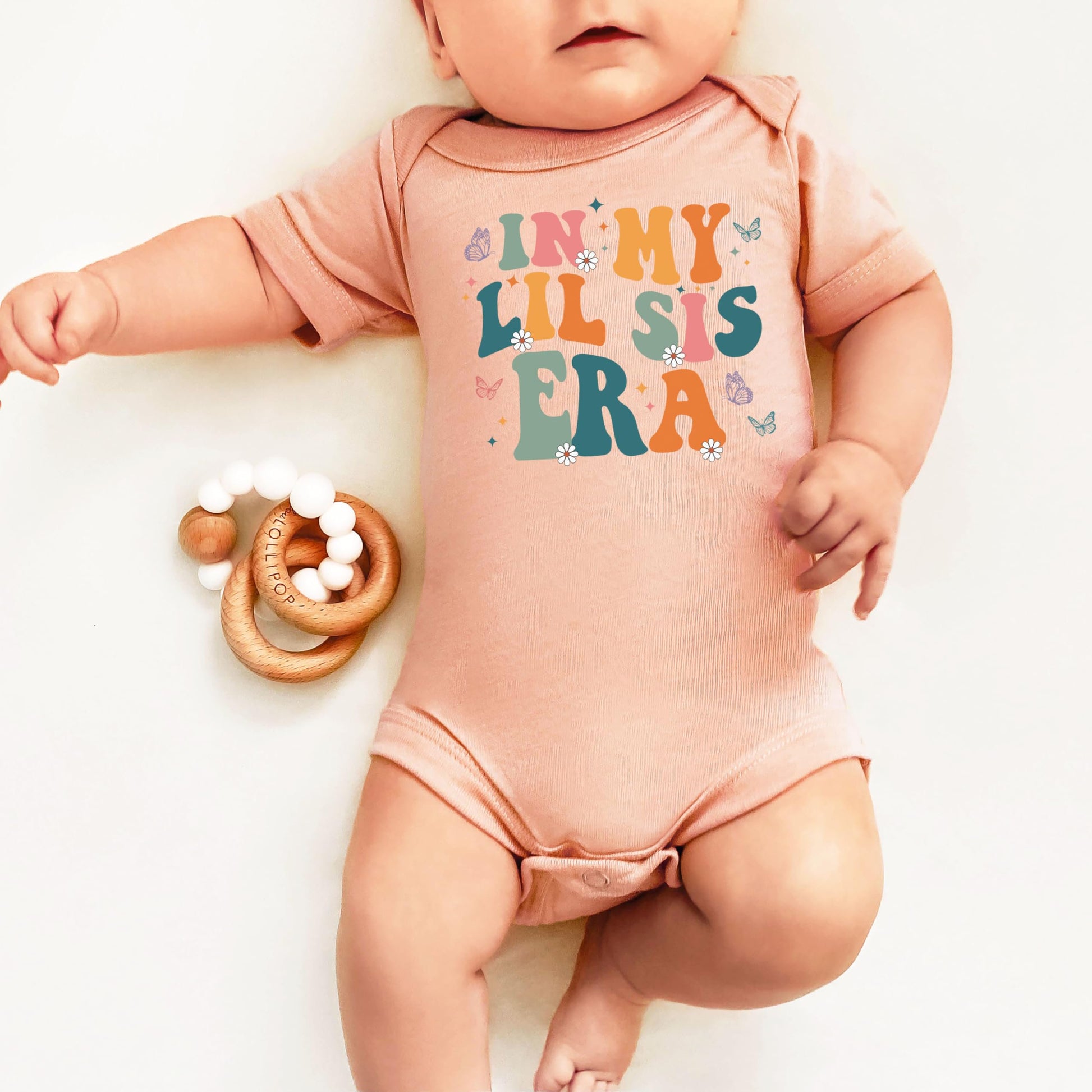 Baby girl wearing In My Lil Sis Era snap-bottom bodysuit with colorful spring butterfly graphic