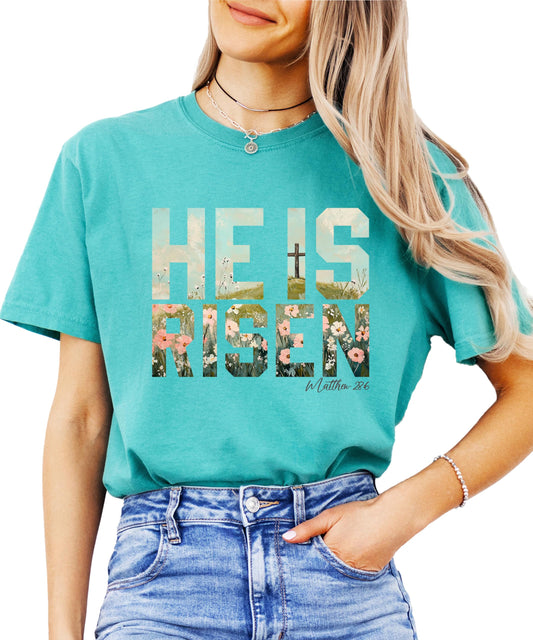 Close-up of He Is Risen floral cross print on women's blue jean graphic tee for Easter