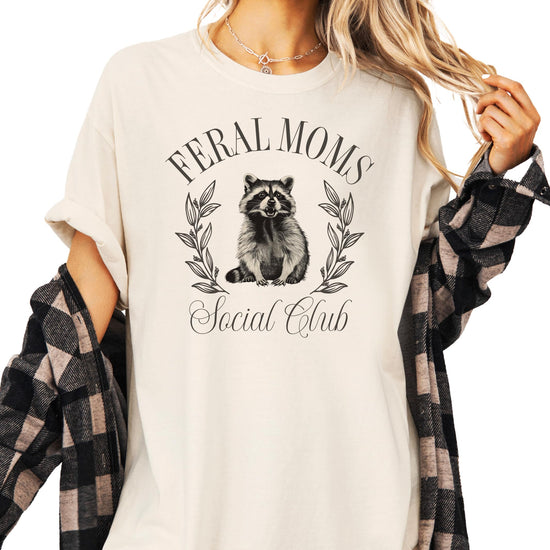 Feral Moms Social Club ivory women's tee with mischievous raccoon graphic and bold text