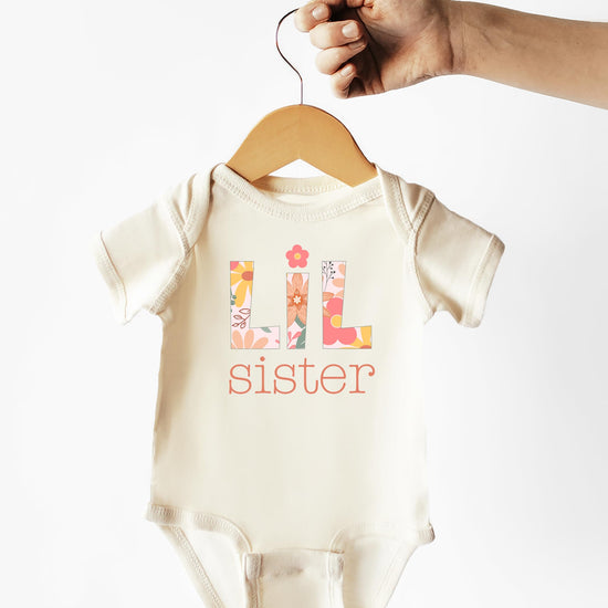 Flat lay of Lil Sister floral baby bodysuit in peach, newborn to 24 months