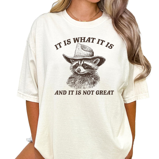 Close-up of the cowboy raccoon graphic and humorous slogan on an ivory women's tee