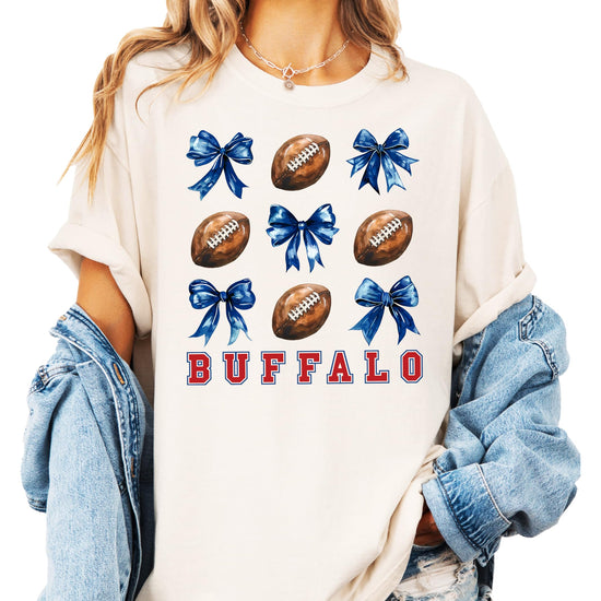 Close-up of Buffalo football shirt print showing red lettering, footballs, and blue coquette bow details