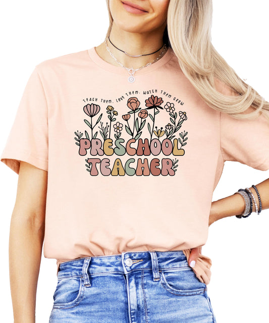 Peach preschool teacher shirt with floral Teach Them Love Them Watch Them Grow design on female model