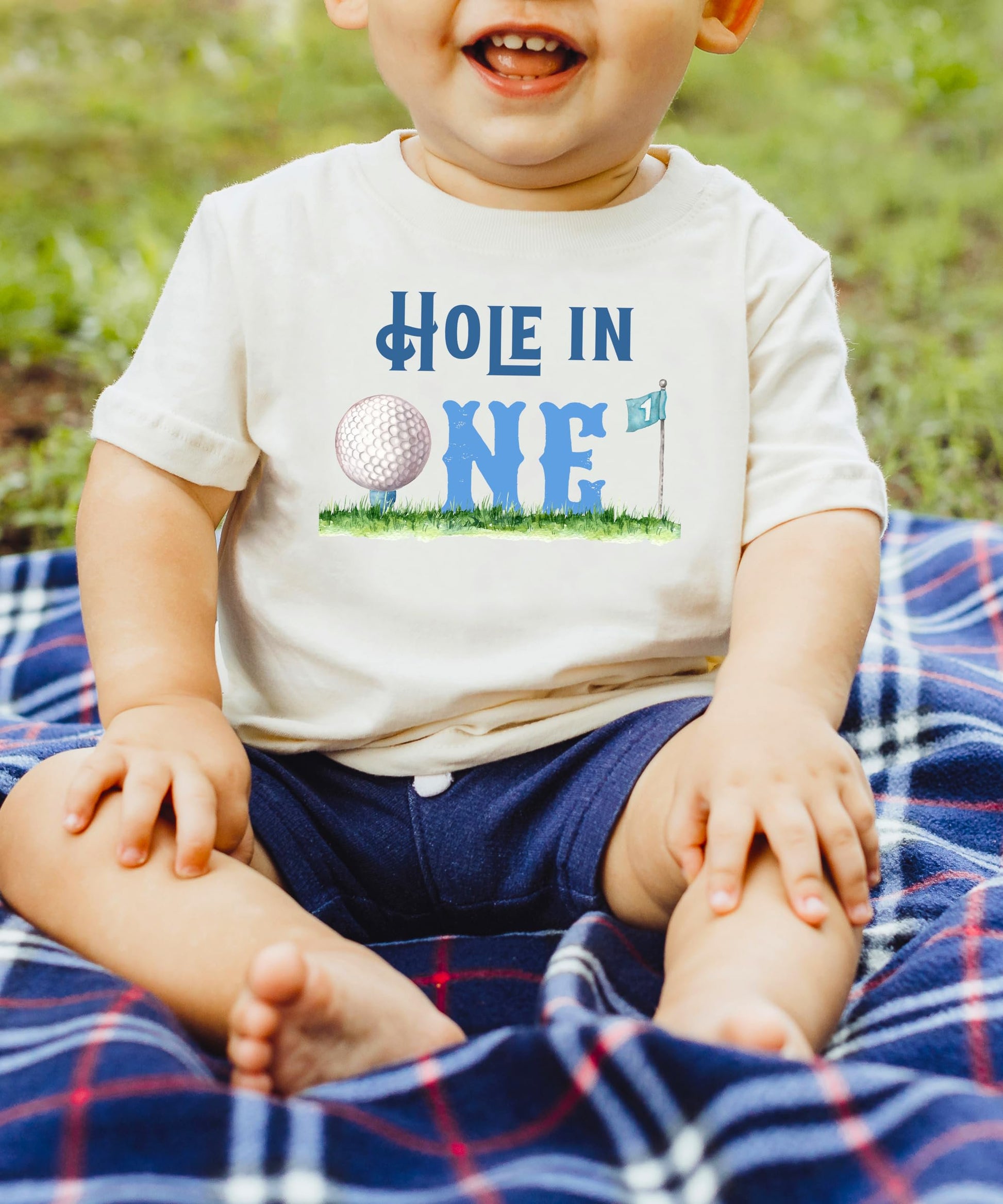Close-up of Hole in One 1st birthday shirt graphic with golf ball and flag print on natural fabric