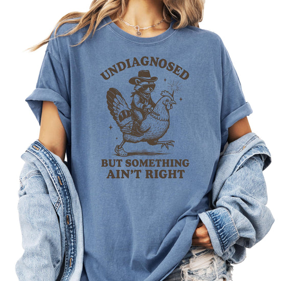 Blue denim style t-shirt with funny raccoon graphic saying Undiagnosed But Something Ain't Right