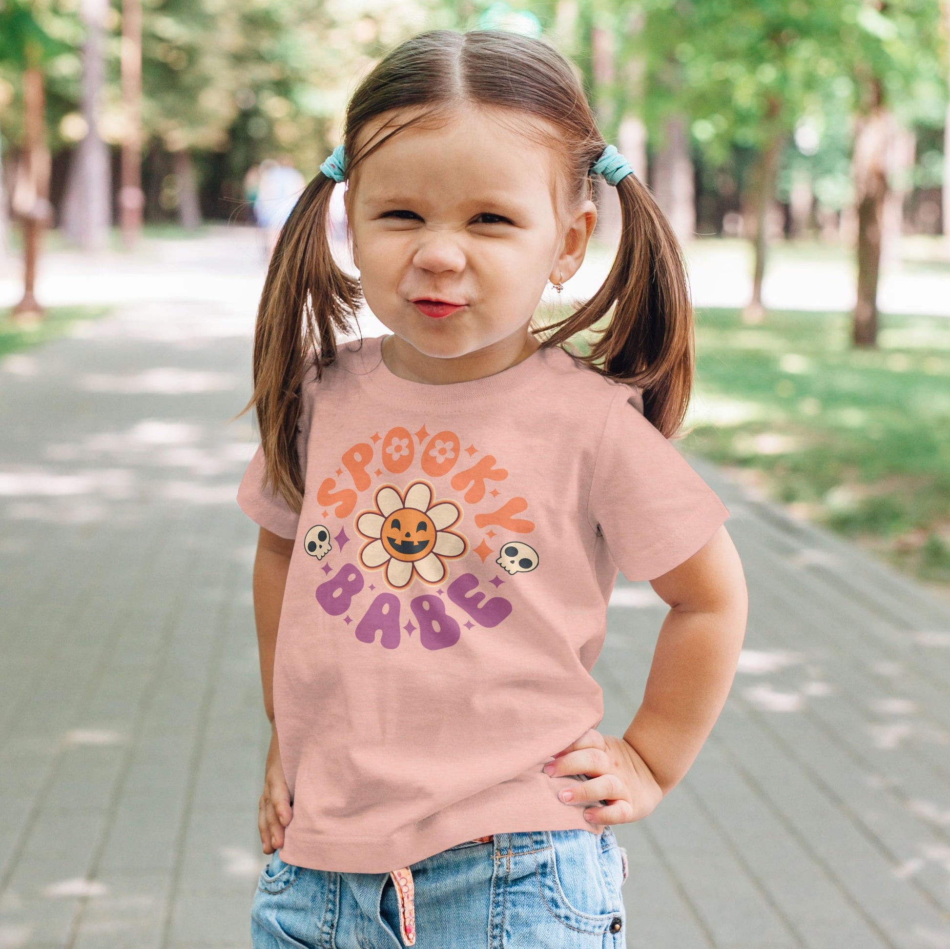 Toddler girl wearing Spooky Babe Pumpkin Halloween tee in peach, full body view