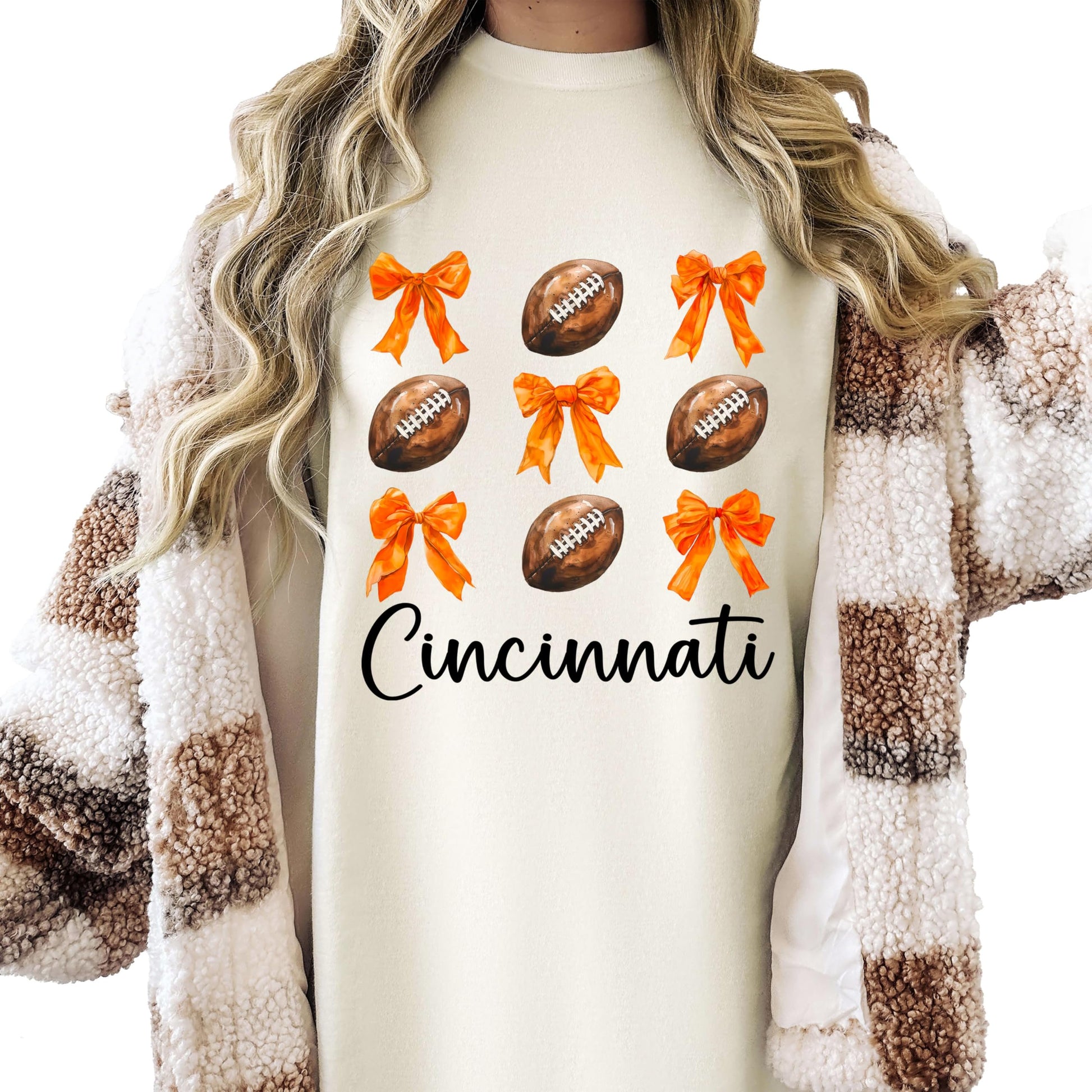 Front view of Cincinnati football girly graphic tee in ivory with orange bow and football print